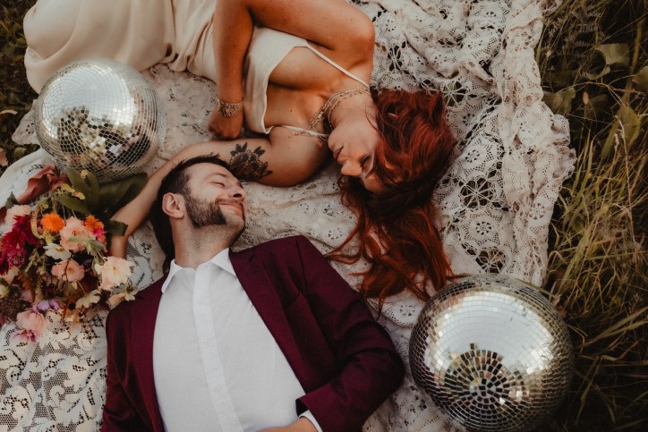 Alternative newlywed couple lying on lace blanket with disco balls and flowers