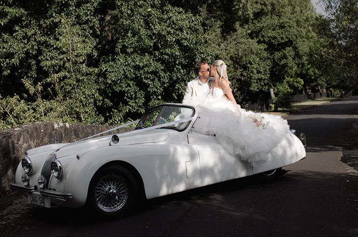 Bride Caitlin and groom kiss in vintage white car