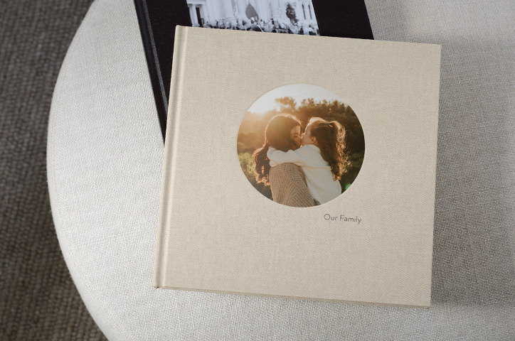 Linen Square Photo Book lying on bed sheets with round picture on cover.