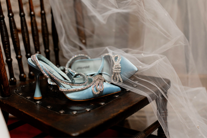 Blue kitten heels with diamond studded bows on a chair next to white mesh veil