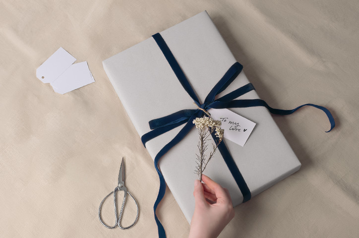 Hand tying a linen giftbox on parchment with silver scissors next to box