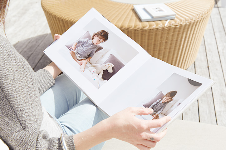 Woman opens a square photo book while sitting on outside deck in sunlight