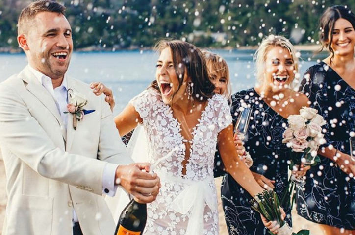 Newlyweds celebrating with champagne at wedding party near ocean