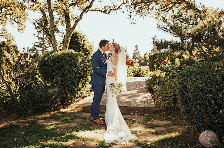 Newlyweds kiss surrounded by hedges in outdoor garden