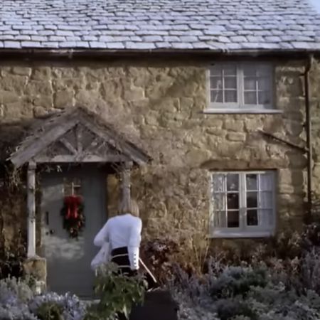 Cameron Diaz has black hair as she poses with Jude Law, who is wearing a gray suit, and Kate Winslet, who is wearing a black dress, as they promote their 2006 movie The Holiday, and a screenshot from the film shows the English Christmas cottage from the film