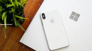 An iPhone resting on top of a Surface PC showing the Microsoft logo.