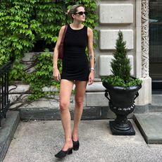 Eliza Huber wearing a black Norma Kamali mini dress with black mules, a burgundy bag, sunglasses, and a slicked back bun.