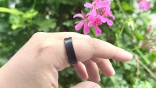 Samsung Galaxy Ring on a person's finger in front of some flowers