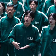 A group of people wearing identical green tracksuits with numbers printed on them, in 'Squid Game' season 2.