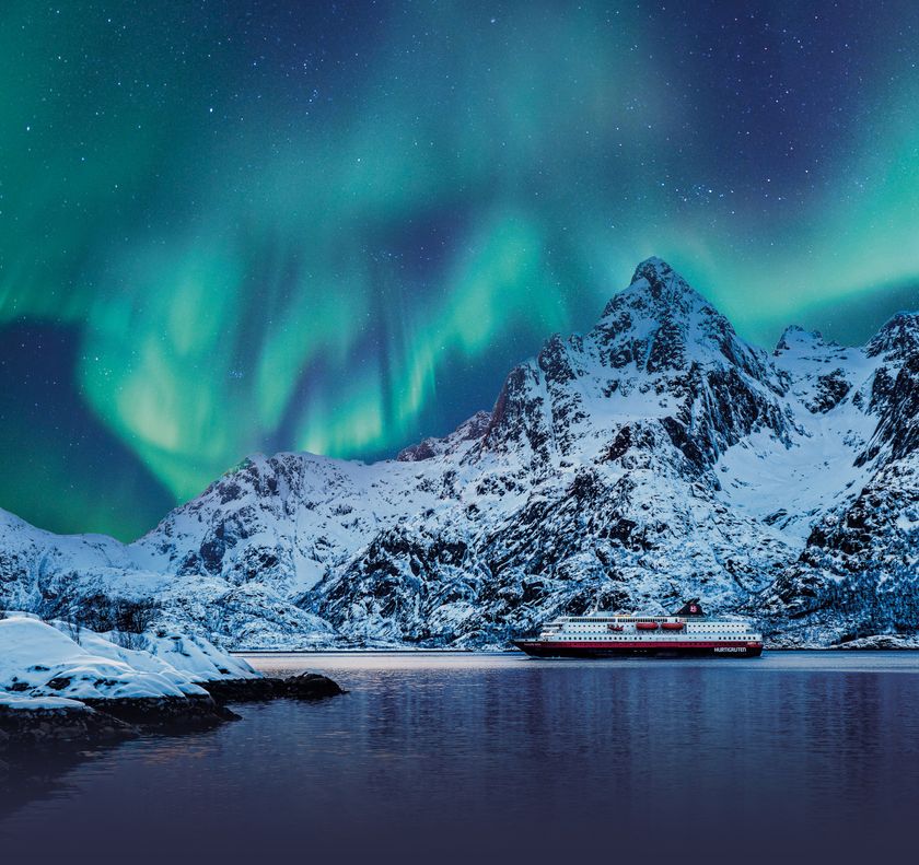 cruise ship next to snowy mountain underneath the northern lights