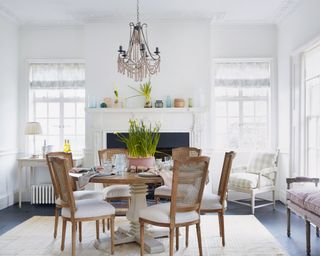 A white dining room with dining table and chairs with the table set for an Easter meal with a bowl of daffodils as a centrepiece.