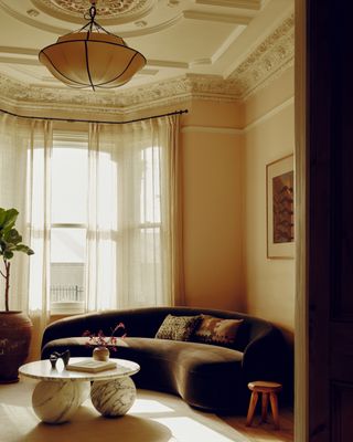 The renovated front room in a period Wimbledon house with a curved sofa and pendant feature light