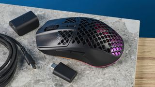 The SteelSeries Aerox 3 on a stone surface and wooden table against a blue background.