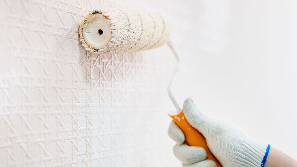 a person painting over wallpaper with a roller