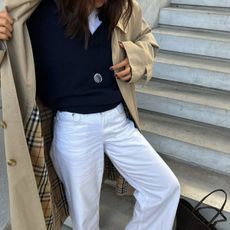 woman in navy sweater, white jeans, and trench coat