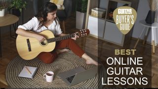 Woman sits on a rug playing guitar in front of her laptop with a pad and pencil next to her