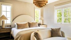 bedroom with rattan light, couch at end of the bed, camel-colored bedding, and arched headboard