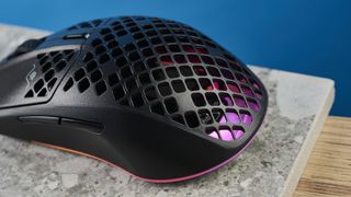 The SteelSeries Aerox 3 on a stone surface and wooden table against a blue background.