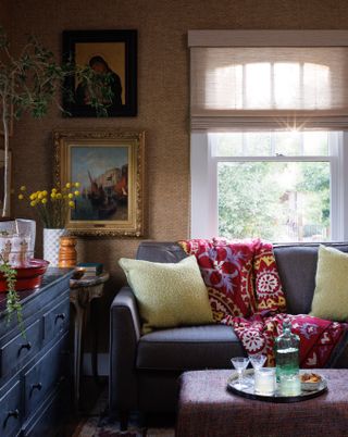 room with beige walls, window, framed artworks, gray sofa with yellow cushions and pink patterned throw