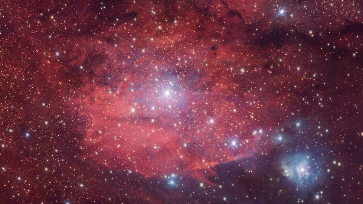 telescope image of a rosy-red nebula in deep space, with bright bluish-white stars in the background.