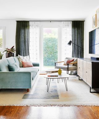 Lounge flooded with natural daylight, featuring hairpin nested tables, blue sofa, and mono full length drapes.