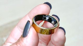 The Samsung Galaxy Ring in a user&#039;s hand with blue painted fingernails