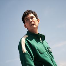 Lee Jung-Jae as Gi-hun, wearing the green tracksuit and standing with the sky behind him, in 'Squid Game.'