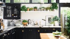 kitchen floating shelves black and white kitchen with marble counterops, black units, brass handles and faucet, white floating shelf with plants, artwork