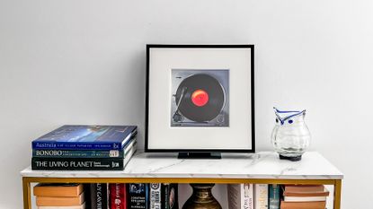 Samsung Music Frame on a table beside some books and a vase