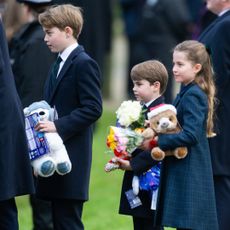 A photo of Prince George, Prince Louis and Princess Charlotte dressed in dark coats and clutching stuffed animals on Christmas