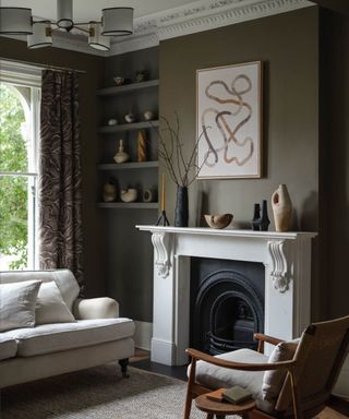 living room with dark green walls, white fireplace, neutral sofa and cozy decor