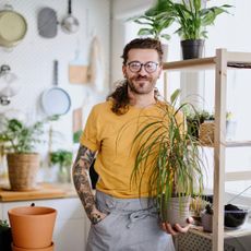 A smiling man with tattoos holding a potted dracaena