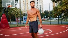 Man holding kettlebell in left hand while standing outdoors