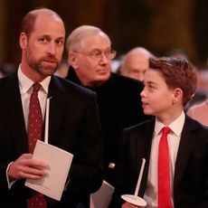 Prince William and Prince George wearing suits and red ties holding candles at a church service and looking at each other