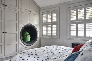 Child’s bedroom with bed with patterned linen, built in wardrobes and reading nook and shutters on windows