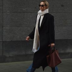 Anouk wears a white scarf, black wool coat, brown leather tote bag, blue jeans, and black sunglasses.