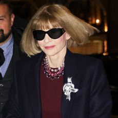 Anna Wintour smiles at the camera wearing black sunglasses