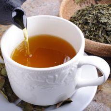 Tea pouring into a teacup next to a bowl of dried herbs