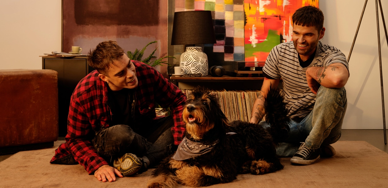 Two men sat on the floor in their home looking at their dog