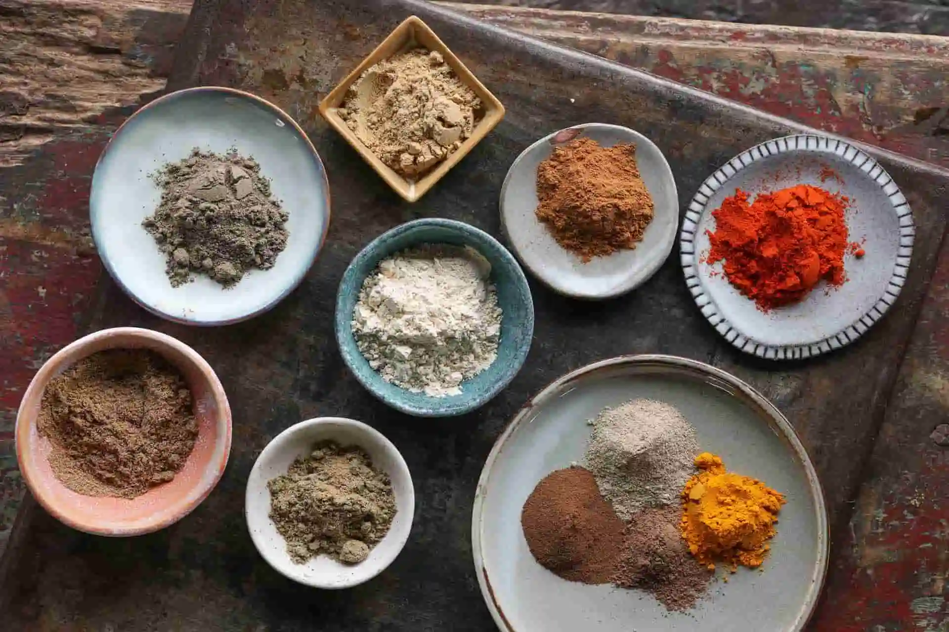 A variety of portioned spices including ground cumin, ground coriander, garlic powder, ground ginger, paprika powder, ground black pepper, ground cinnamon, ground cardamom, ground turmeric, ground allspice, and ground cloves. 