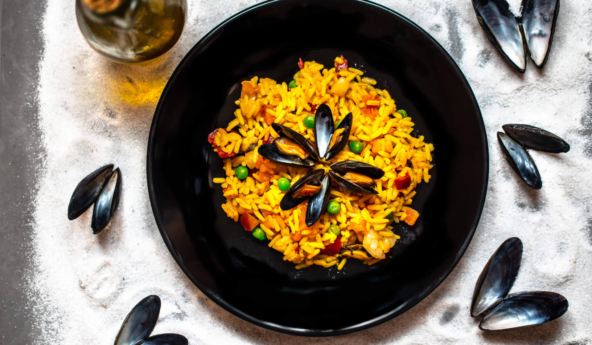 Spanish paella from above with yellow rice, green peas, and clams in a black bowl