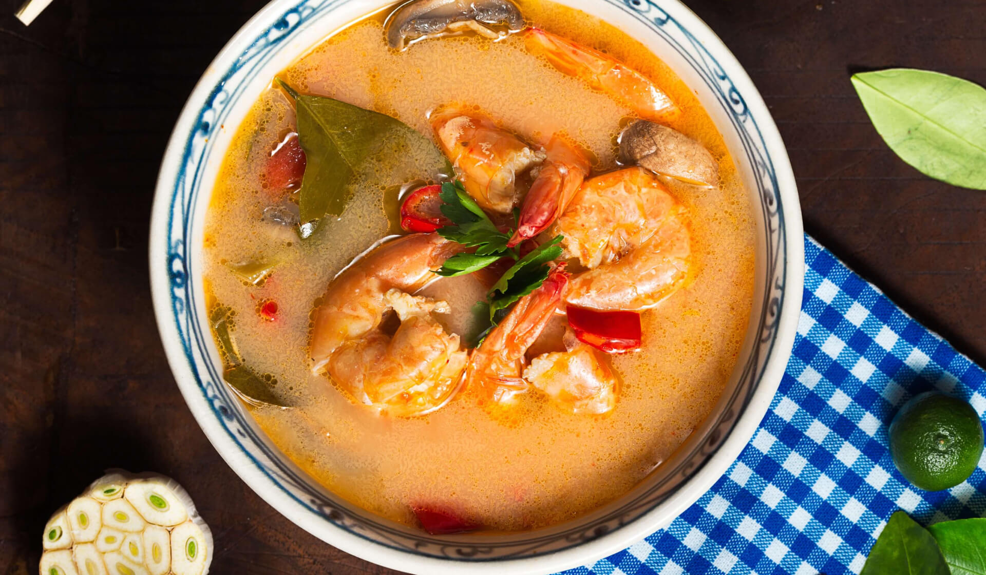 Thai tom yum soup with a redish broth, shrimp, mushrooms, Thai basil, and parsley