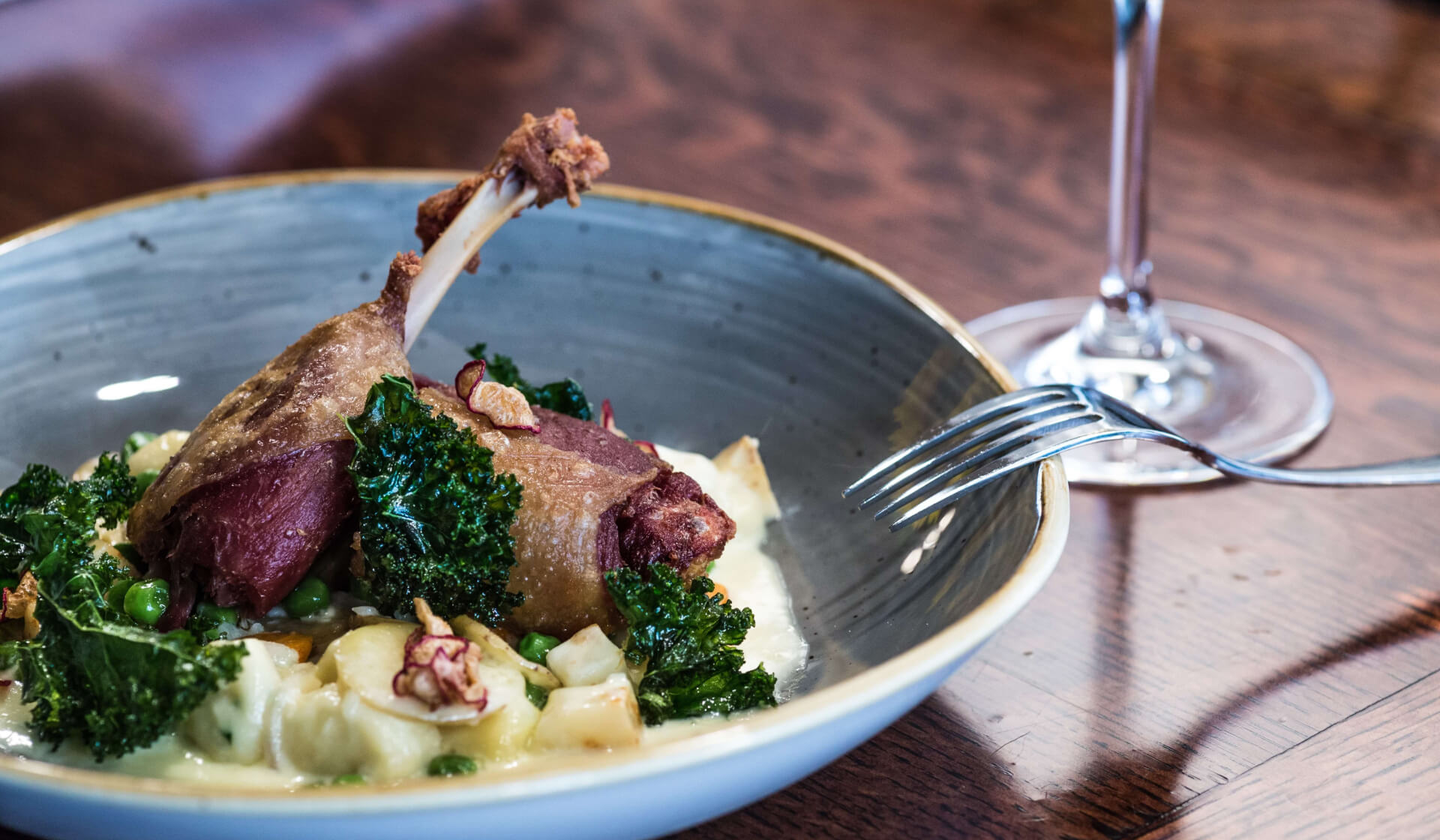 Bowl filled with French duck confit with potatoes and kale and a fork resting over the bowl