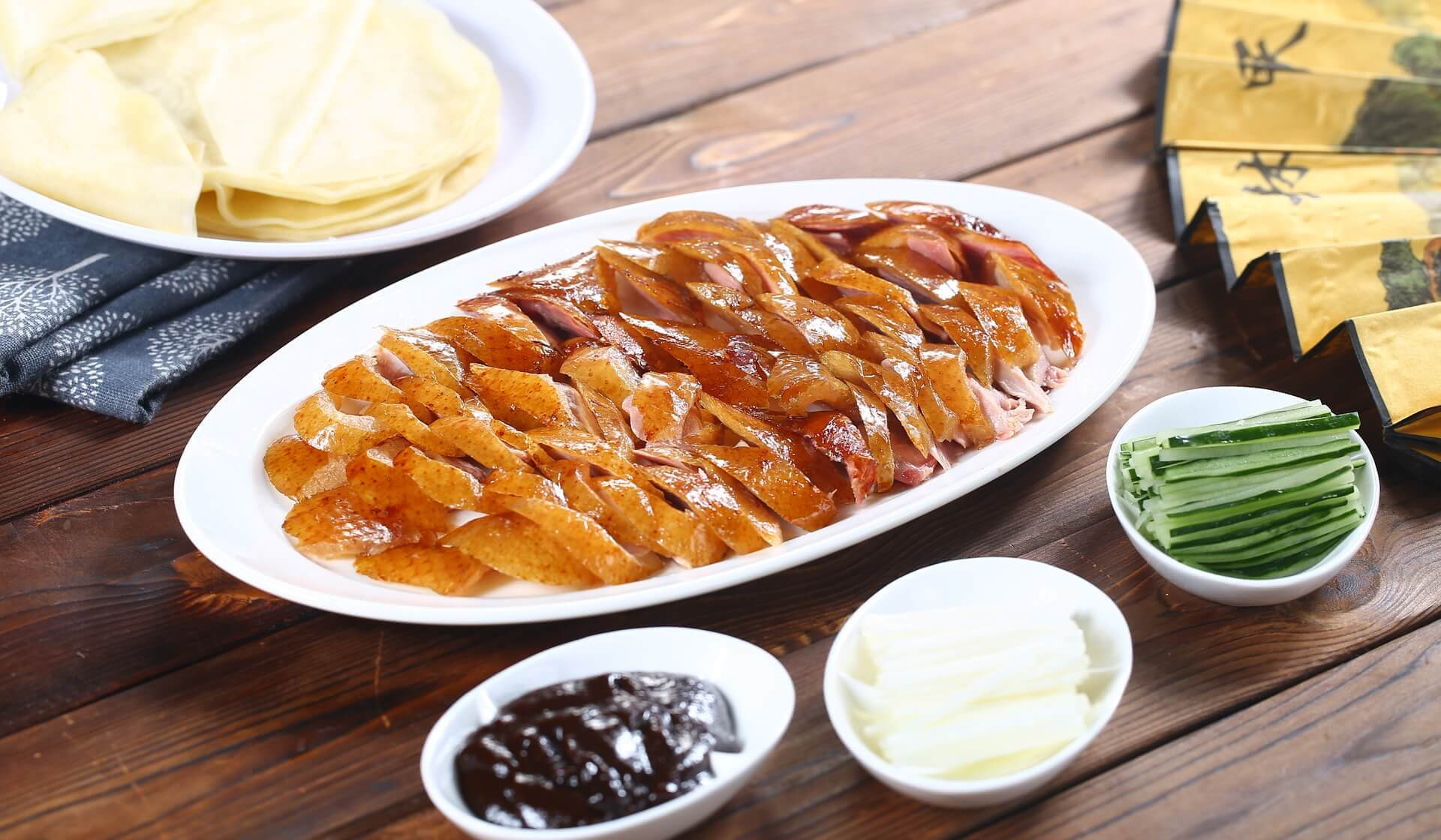 Chinese peking duck on a play on a table with rice paper wraps and cucumber slices and plum saucee