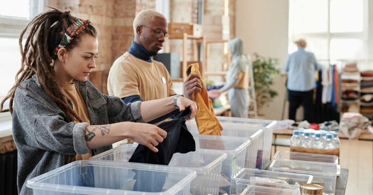 Two people volunteer, folding clothes and placing them in clear bins