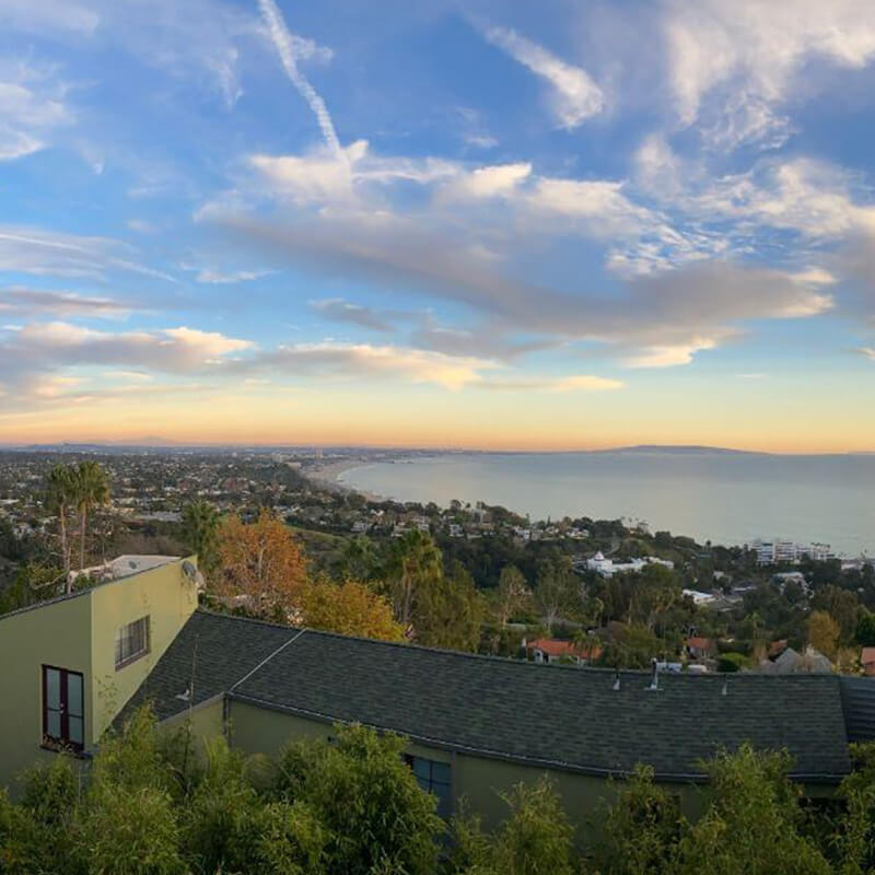 Scenic coastal view of a hillside neighborhood overlooking the ocean at sunset with a colorful sky.