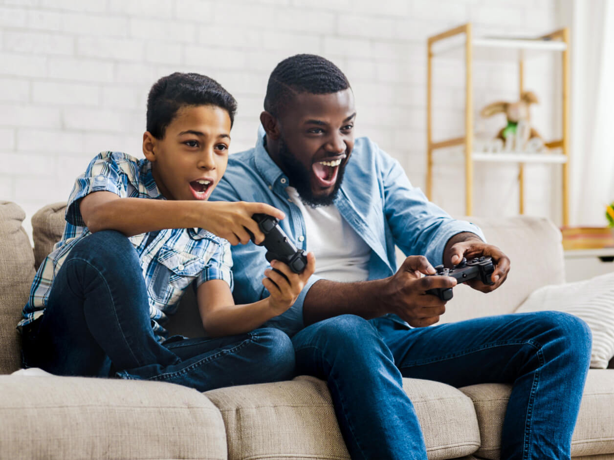 Adult and child enjoying video games together on the couch.