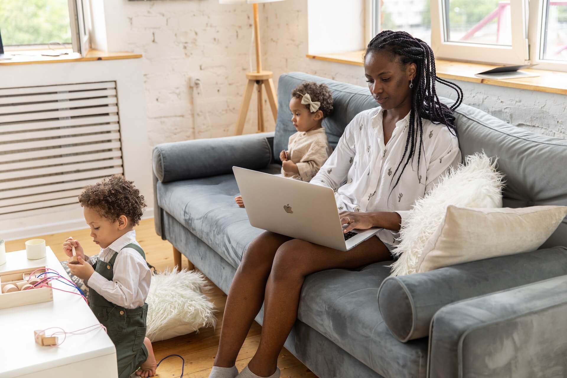 A family gathered in a living room while the mom is working online on her Macbook.