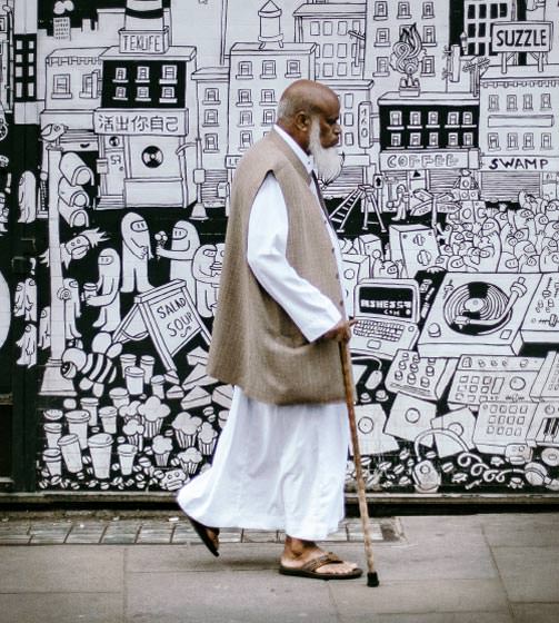 Older man walking with cane in front of black and white mural