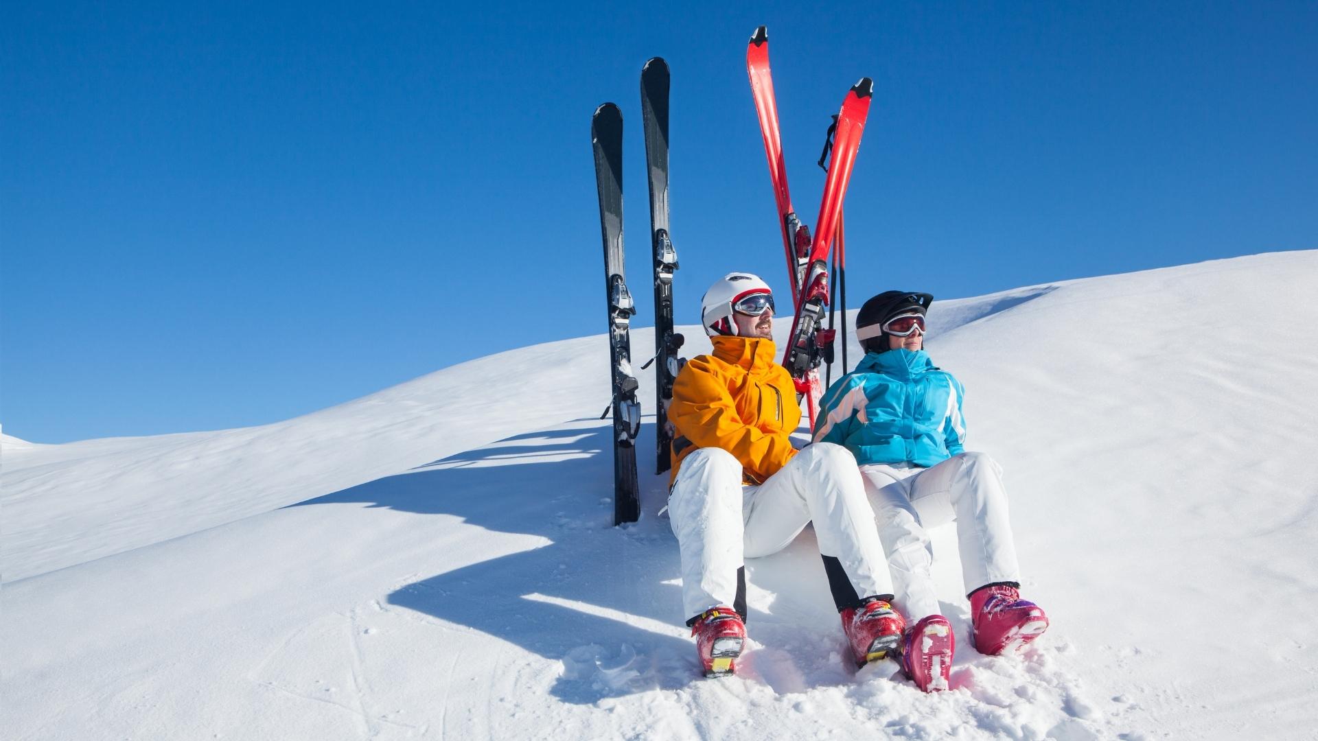 Two people sat on a snowy mountain with their skis